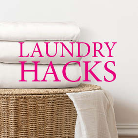 A wicker basket with 3 white folded clean sheets on top and the words Laundry Hacks in pink over it
